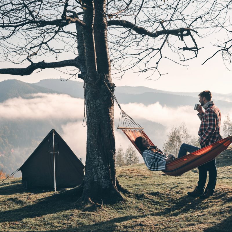 What is our next travel destination? Attractive young woman lying in hammock while her boyfriend standing next to her